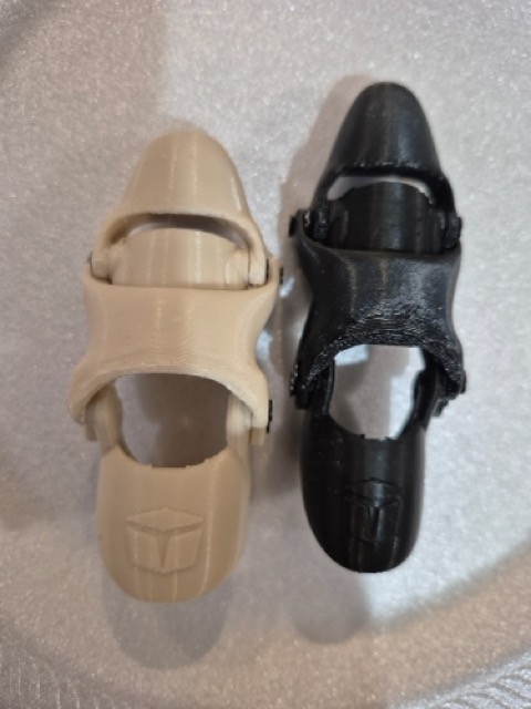 Two prosthetics side by side on a white surface, beige and black versions showing the iteration progression